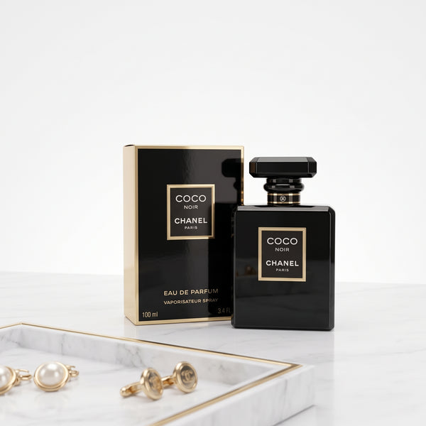 Chanel Coco Noir Eau de Parfum 100ml bottle and its black and gold packaging box, styled on a white marble tray with gold cufflinks against a clean white background.