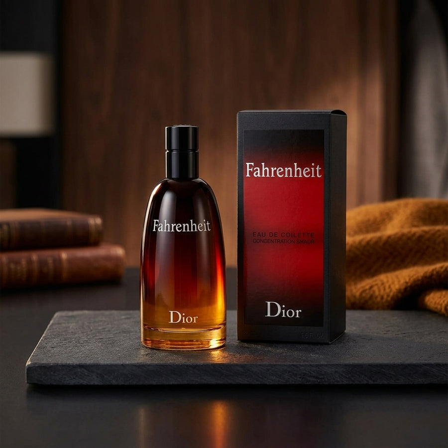 Dior Fahrenheit Eau de Toilette bottle with a black cap next to its black and red retail box, displayed on a dark stone slab with a warm, blurred background.