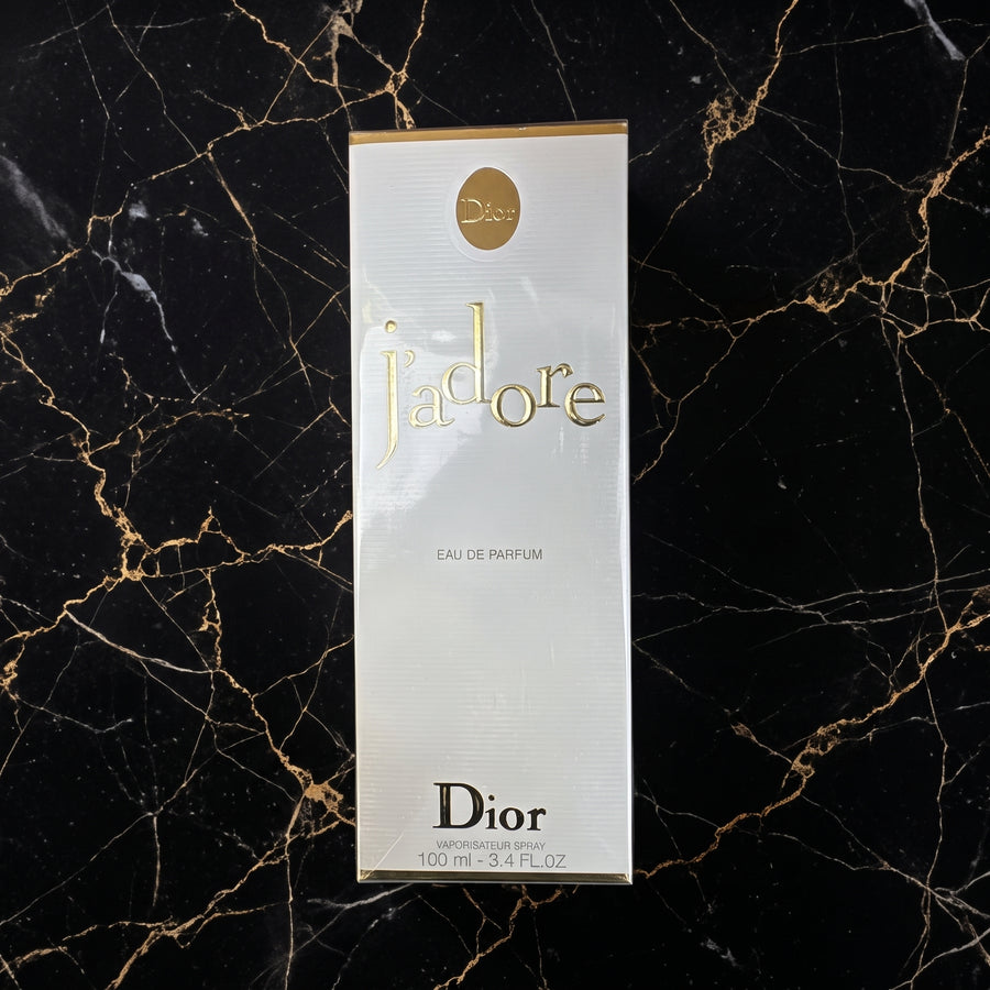 Dior J'adore Eau de Parfum 100ml box on a black marble background with gold veining.