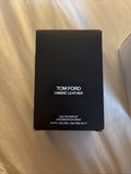 A black rectangular box of Tom Ford Ombre Leather Eau de Parfum, photographed on a beige fabric surface.