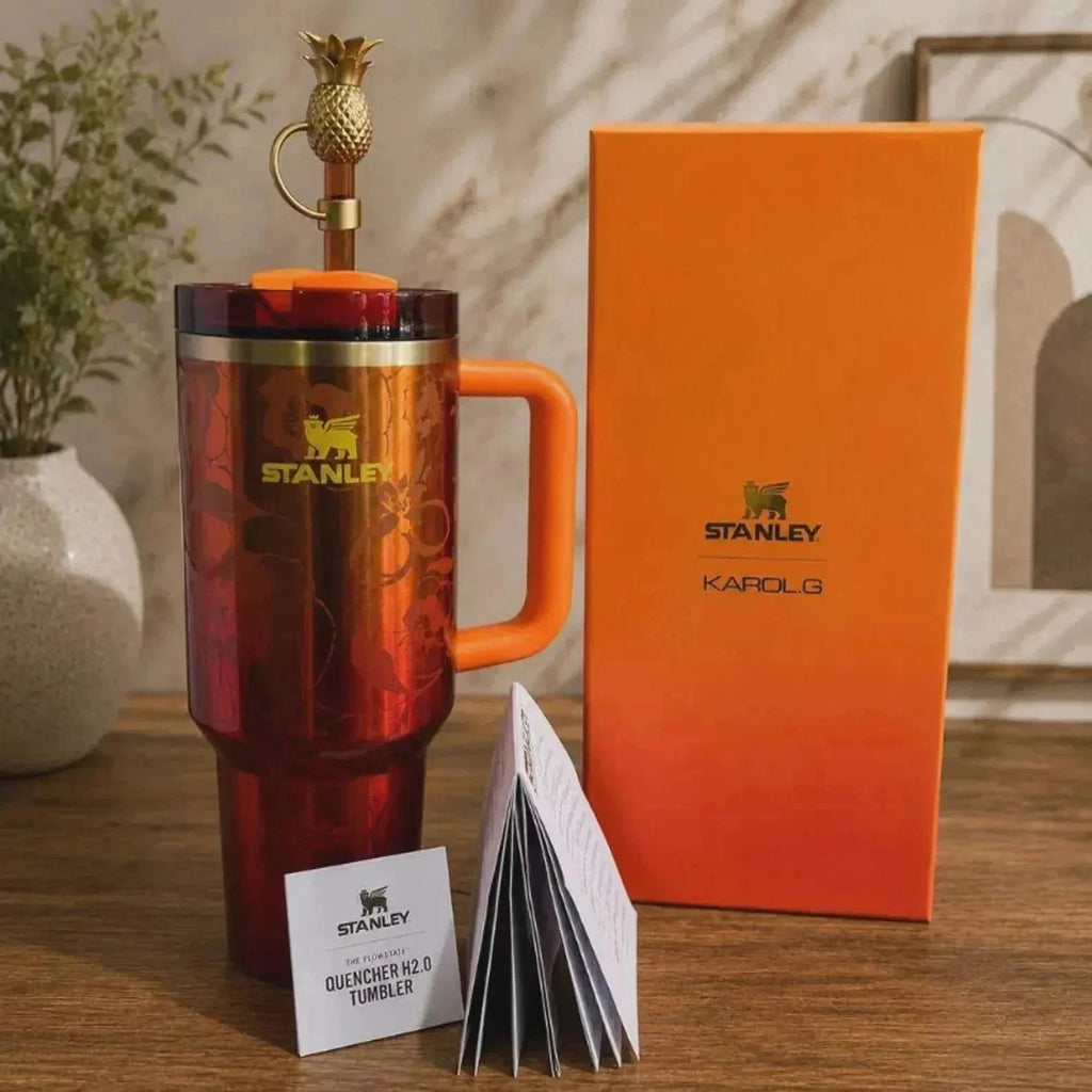Stanley Karolo 32 oz chevron stainless steel tumbler in a red and orange gradient finish, shown with its orange packaging box and branded card on a wooden table.