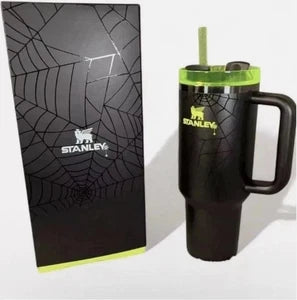 A black handled tumbler with a green lid and straw, shown next to its black packaging box featuring a spiderweb design.