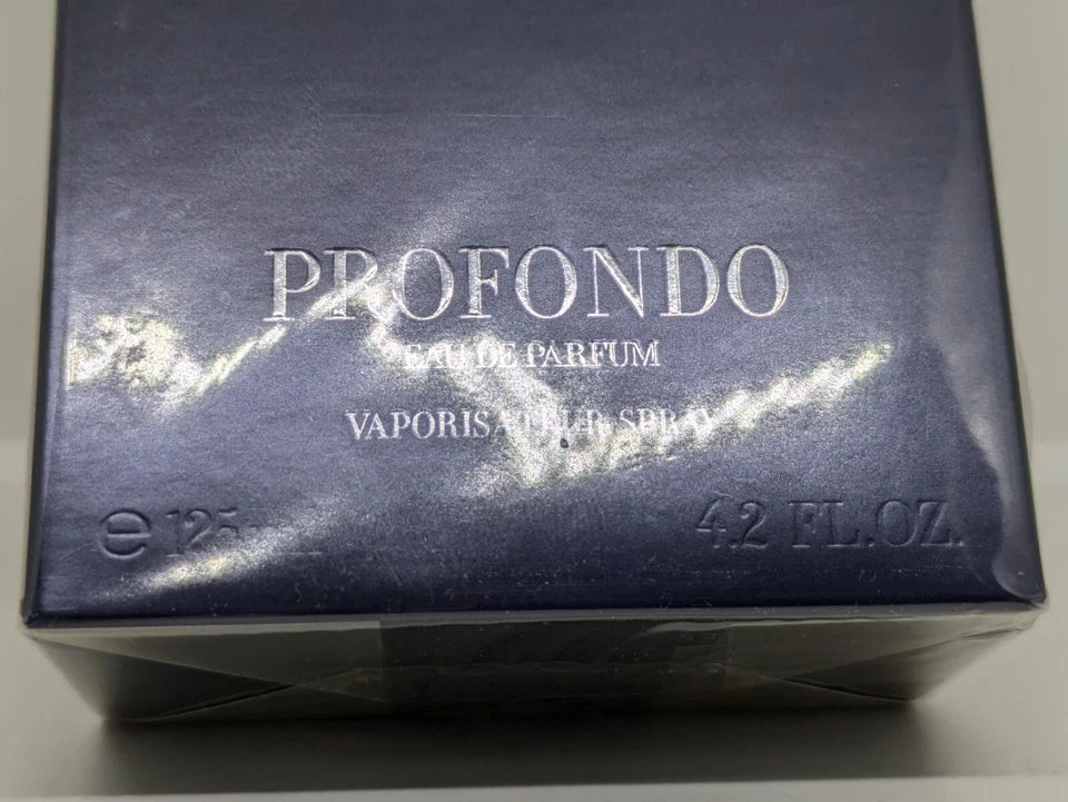 A square blue perfume box with the word 'PROFUNDO' in large white letters and a silver-toned horizontal band across the center, photographed against a dark background.