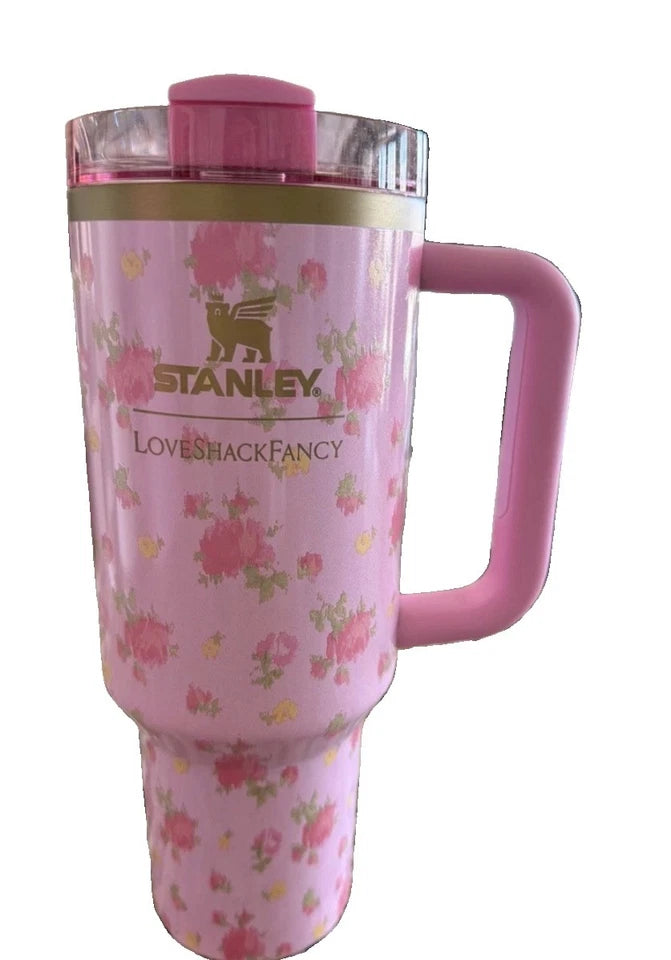 A pink Stanley travel tumbler with a floral pattern, featuring a pink handle, clear lid, and gold Stanley logo on a white background.