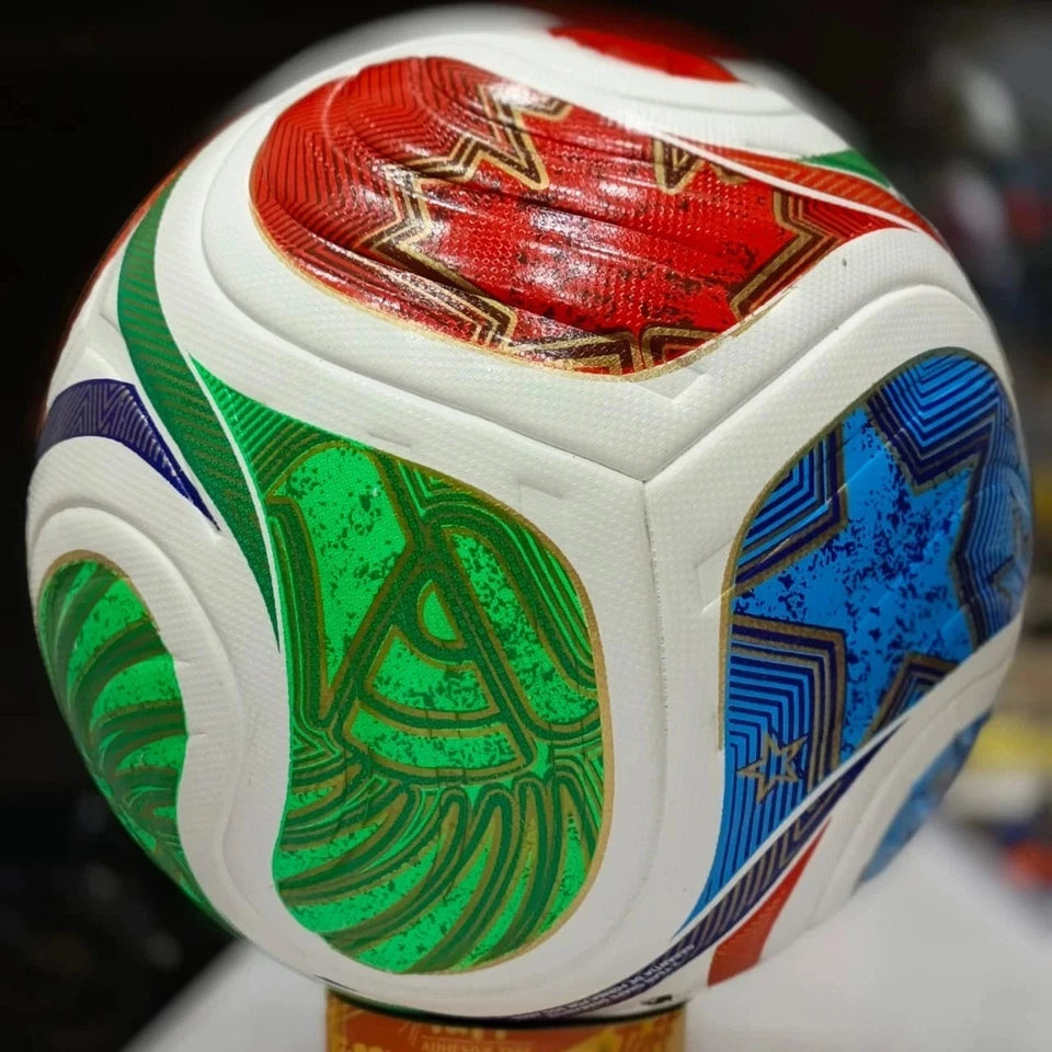 A close-up of a soccer ball with white panels and vibrant green, blue, red, and purple graphic patterns outlined in gold.