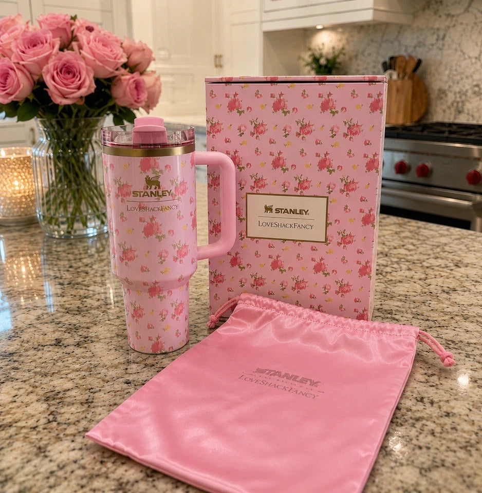 A pink Stanley travel tumbler with a floral pattern, shown with its matching pink storage bag and branded box on a granite countertop in a kitchen setting.