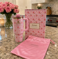 A pink Stanley travel tumbler with a floral pattern, shown with its matching pink storage bag and branded box on a granite countertop in a kitchen setting.