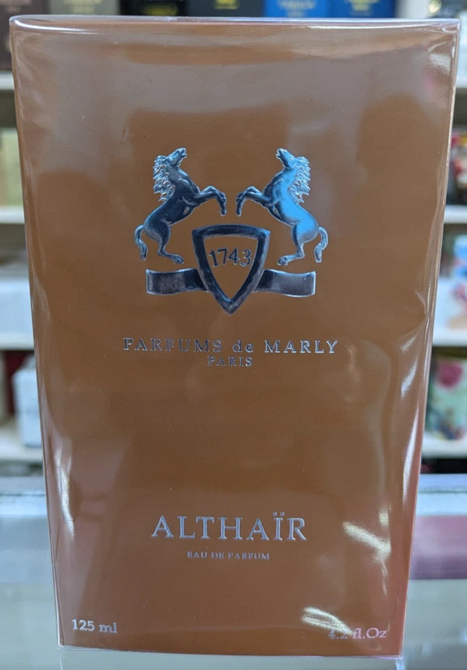 A 125 ml bottle of Althačr Eau de Parfum by Parfums de Marly, shown in its original clear plastic retail box packaging. The packaging features a warm brownish-gold background with a silver crest of two rearing horses and the brand name printed in silver.