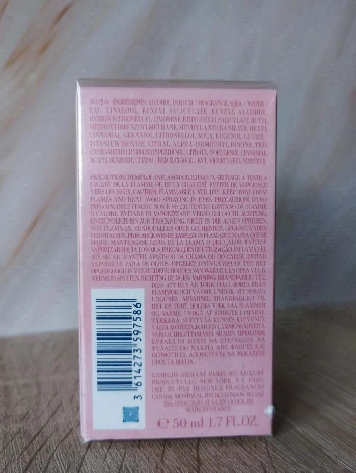 The back of a pink cosmetic box, showing extensive ingredient text in Spanish and a barcode, placed on a light-colored wooden surface.