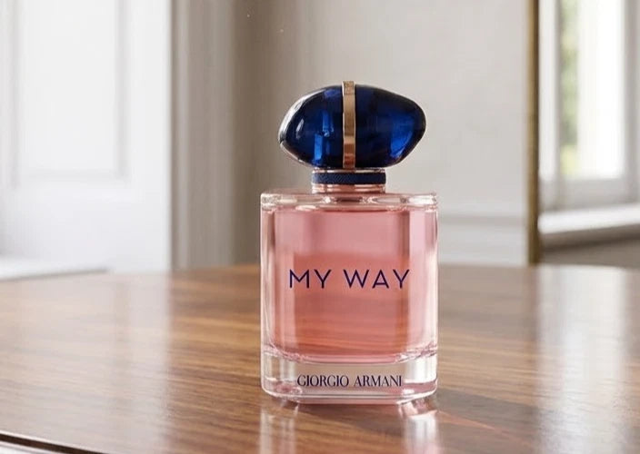 A bottle of Giorgio Armani My Way Eau de Toilette perfume with pink liquid and a dark blue cap, sitting on a wooden table in a softly lit indoor setting.