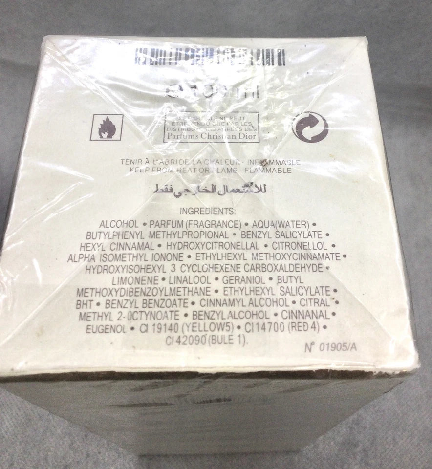 The back of a perfume box wrapped in clear plastic, showing product details, ingredients, and barcode information on a gray fabric background.